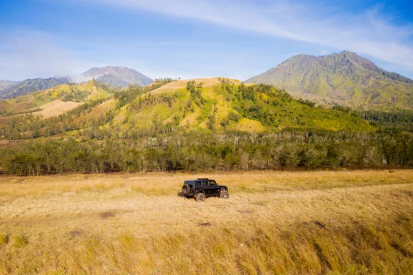 越野车在有山地背景的干枯草地上行驶的美丽的空中风景 — 图库照片
