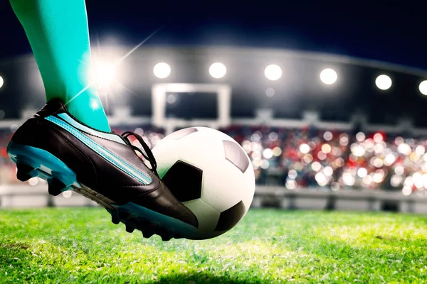 Close up of a soccer player feet kicking a ball with powerful toward a goal while playing on a stadium with crowds spectators background