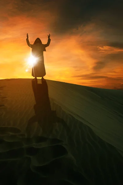 夕日を背に砂丘の上に立ち アラビア人のシルエットが手を挙げて アッラーに祈っている — ストック写真