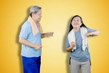 Stüdyoda dans ederken spor kıyafeti giyen mutlu çift sarı arka planda.