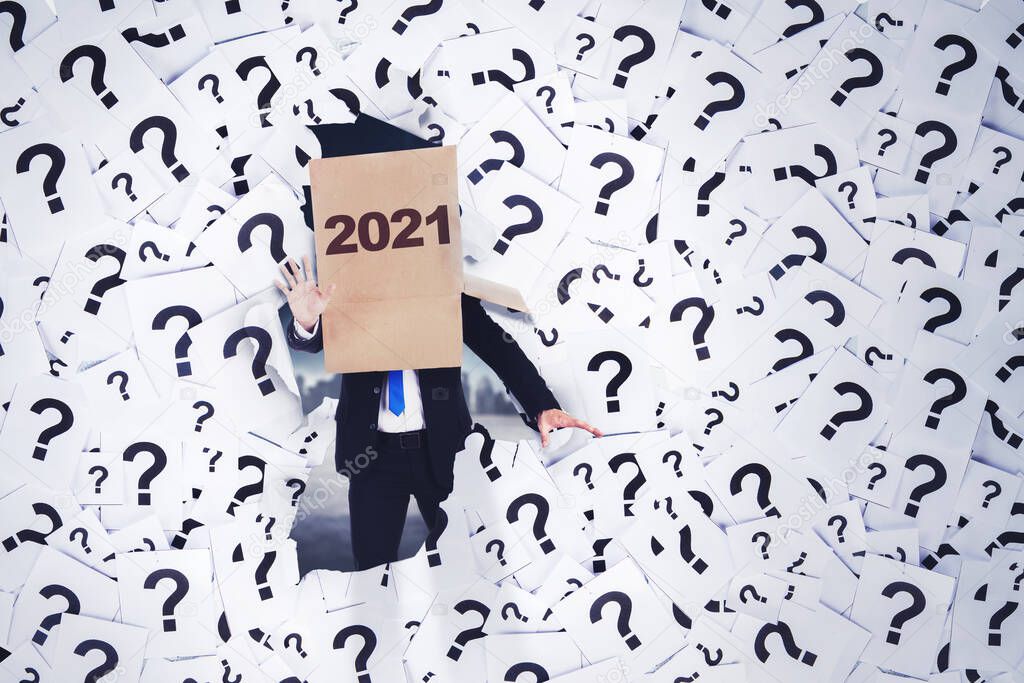 Disoriented businessman wearing cardboard with 2021 numbers on his head while walking with question marks symbol background