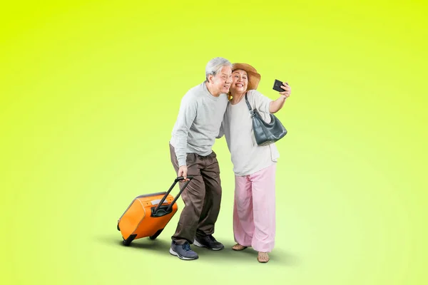 一对快乐的老夫妇一边带着行李 一边用智能手机在有绿色屏幕背景的工作室里合照一张自拍照 — 图库照片