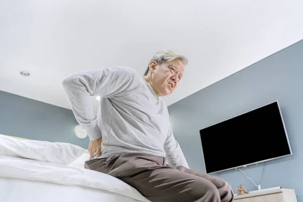 老年人在床上坐着醒来后背痛的低角度图像 在家里中弹 — 图库照片
