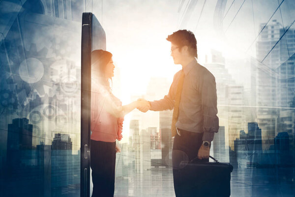 Double exposure of two business people shaking hands after online meeting by using mobile phone with modern city background
