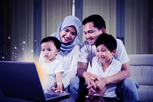 快乐的穆斯林家庭在客厅里坐在沙发上 用一台装有闪光监视器的笔记本电脑 在家里中弹 — 图库照片