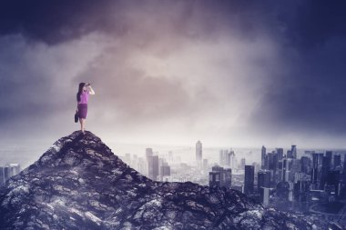 Portrait of female manager using binoculars to looking at the stormy in a city while standing on the peak of mountain