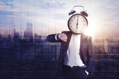 Çalar saatin başındaki işadamının, şehir manzarasını yansıtan cam pencerelerle kol saatine bakarken iki kez görüntülenmesi.