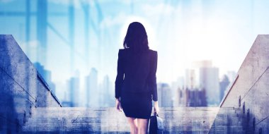 Rear view of female manager carrying a suitcase while climbing stairs with modern city background