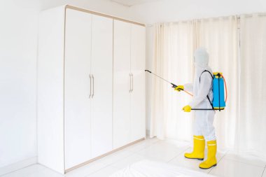 Koruyucu giysi giyen erkek işçi, hasta evindeki dezenfektan spreyiyle gardırobu temizlerken ve koronavirüs hastalığını temizlerken