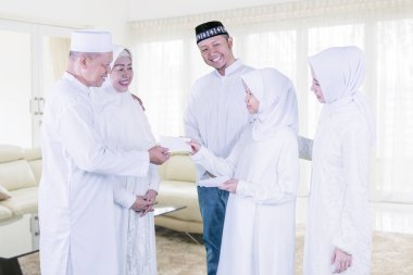 Üç kuşak mutlu Müslüman aile, evde Mübarek bayramında oturma odasında dururken küçük kıza para zarfı veriyor.