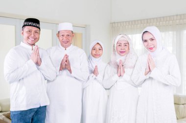 Üç nesil Müslüman aile, oturma odasında yan yana dururken bayram jesti yapıyor. Evde vuruldu.