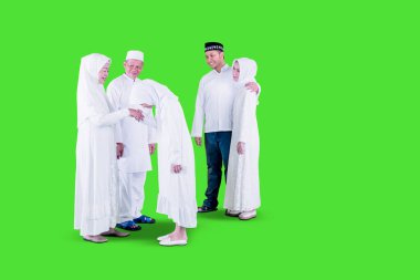 Müslüman küçük bir kız, yeşil perdeli bir stüdyoda bayram boyunca ebeveynlerinin yanında dururken dedelerinden özür diliyor ve tokalaşıyor.