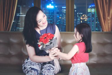 Genç anne, kızından çiçek alırken mutlu görünüyor ve gece şehir arka planına sahip bir kanepede oturuyor. Apartmanda vuruldu.