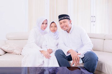 Mübarek bayramda kanepede yan yana otururken kameraya gülümseyen genç Müslüman bir aile. Evde vuruldu.