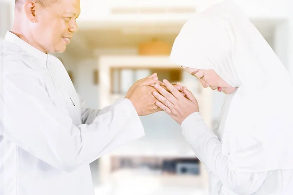 Side view of Muslim old couple handshaking and forgiving to each other during Eid Mubarak in the living room. Shot at home