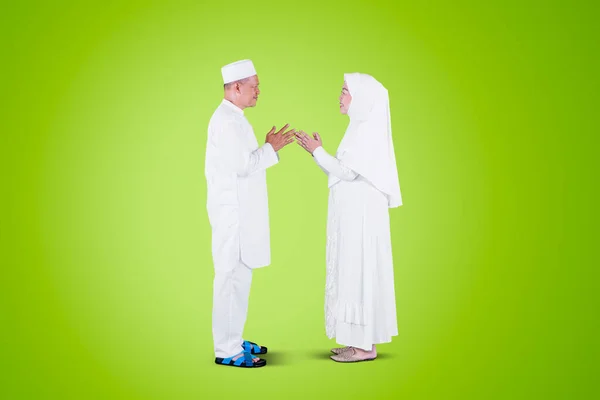 Side view of Muslim old couple handshaking and forgiving to each other during Eid Mubarak in the studio with green screen background