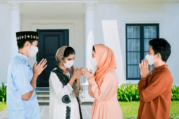 Four young people wearing face mask while give greet hands to forgive each other during Eid Mubarak celebration in the house yard