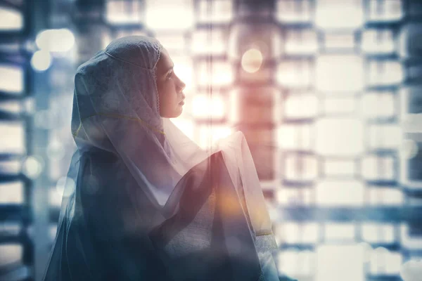Side view of religious woman praying to the Allah while sitting in the mosque with blurred sunlight sparkle background