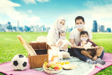 Şehir planında birlikte piknik yaparken yüz maskesi takan Müslüman bir aile.