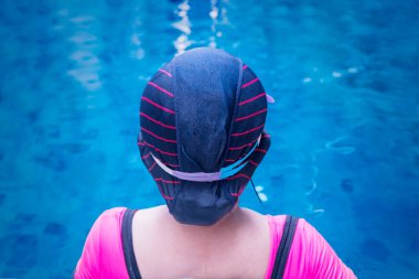 Havuz kenarında mavi arka planda oturan, mayo giyen yaşlı bir kadın.