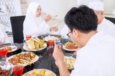 Mübarek bayramında evde yemek yiyen üç kuşak mutlu Müslüman aile.