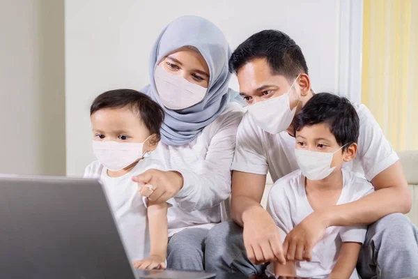 Muslim family wearing face mask while using a computer laptop together in the living room during quarantine at home