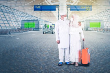 Bayramda havalimanında bavul tutarken ve yan yana dururken maske takan yaşlı Müslüman bir çift.