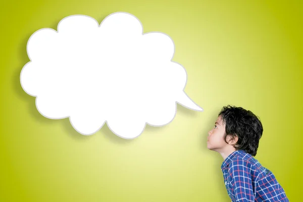 一个小男孩站在有黄色背景的演播室里看着一个空洞的云彩演讲泡沫的侧视图 — 图库照片
