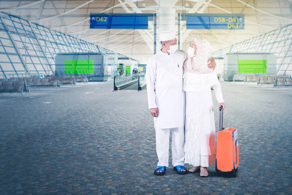 在开斋节期间 穆斯林老两口带着面具 提着行李 站在机场 — 图库照片