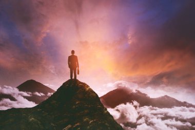 Tepelerde durup sisli dağa bakarken erkek yöneticinin bavul taşıdığı arka manzara. Güneş doğarken çekilmiş.