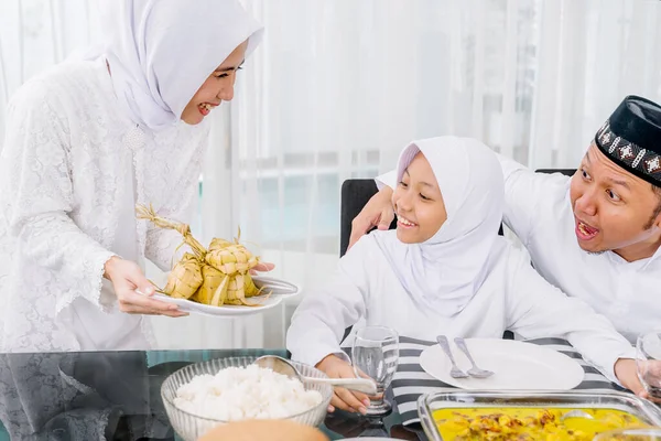 若い女性は 自宅でEid Mubarak中に夕食を食べながら ダイニングルームで彼女の家族のために伝統的な食品Ketupatを提供 — ストック写真