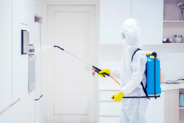 家の台所で消毒剤を噴霧しながら保護服を着ている若い男は コロナウイルスのパンデミックの間に — ストック写真