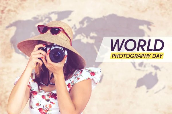 Female tourist using digital camera while standing with world photography day text and world map background