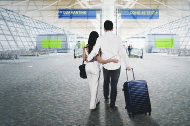 Back view of young couple looks confused while standing between directions of quarantine or Covid-19 test in the airport