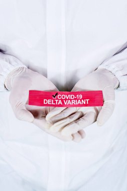 Close up of medical worker hands holding a paper with Covid-19 Delta variant text while wearing hazmat suit clipart