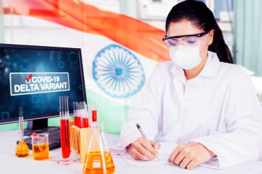 Female scientist analyzing sample of covid-19 delta variant while sitting with India flag in the laboratory
