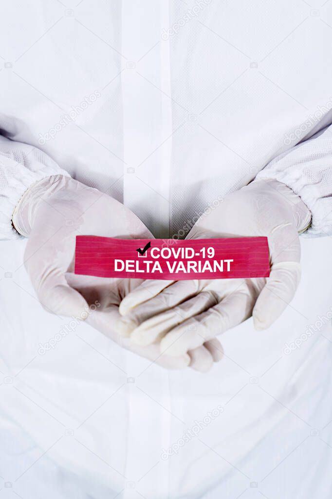 Close up of medical worker hands holding a paper with Covid-19 Delta variant text while wearing hazmat suit