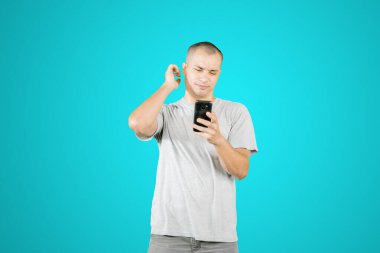 Confused young man reading bad news on his mobile phone while standing in the studio with tosca background
