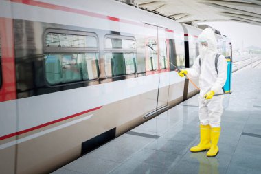 Young man wearing Hazmat suit while spraying disinfectant to the train in station during coronavirus pandemic