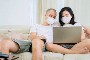 Young couple using a laptop computer together on the couch while wearing face mask during self isolation at home