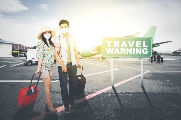 在机场航站楼的路标上 一对年轻夫妇戴着口罩 站在路标上写着旅行警告 — 图库照片
