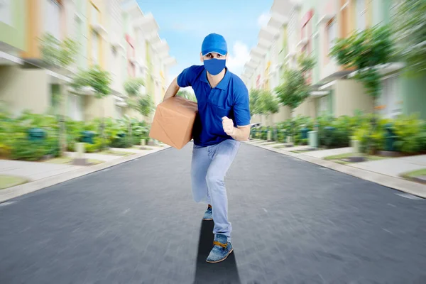 男快递员戴着面具 一边跑一边送包裹给顾客 — 图库照片