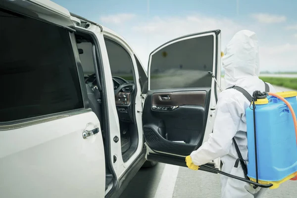 道路脇の車室内に消毒剤を噴霧しながら防護服を着た男性労働者によるコロナウイルス感染防止 — ストック写真