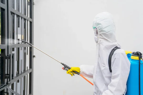 コロナウイルスのパンデミック時に家のフェンスに消毒剤を噴霧しながらハズマットスーツを身に着けている男性労働者 — ストック写真