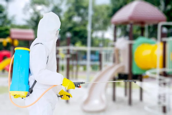 コロナウイルスのパンデミックの間に遊び場で消毒剤を噴霧しながら保護服を着ている若い男の写真 — ストック写真