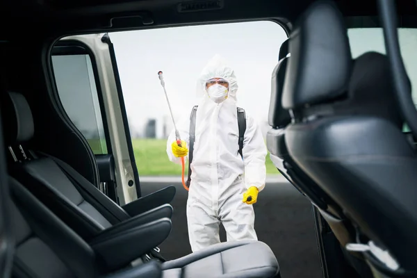 道端で車内に消毒剤を噴霧しながら保護服を着た若者がコロナウイルスの感染を防ぐ — ストック写真