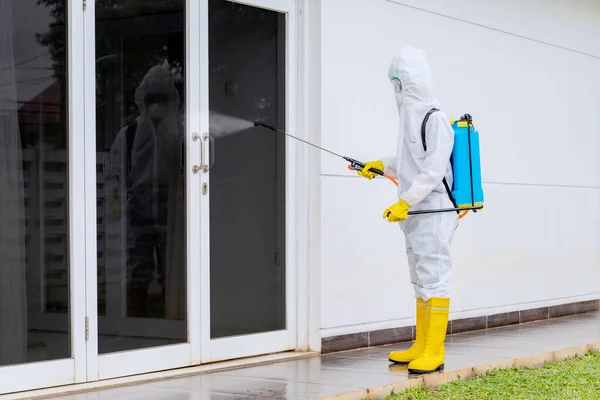 コロナウイルスのパンデミックの間に病院のガラスドアに消毒剤を噴霧しながら保護服を着ている若い男 — ストック写真