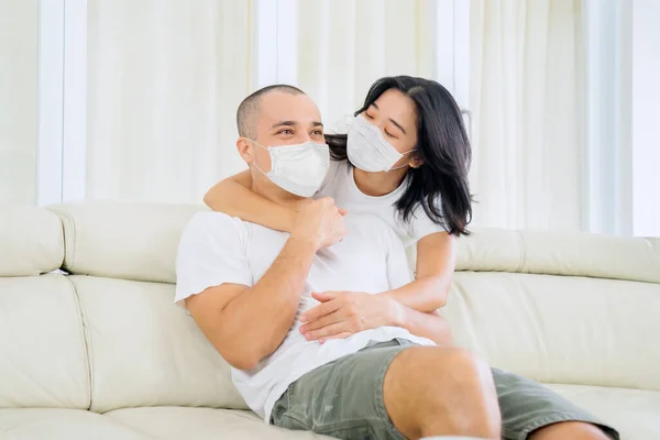 Young Woman Embrace Her Husband Couch While Wearing Face Mask — Zdjęcie stockowe