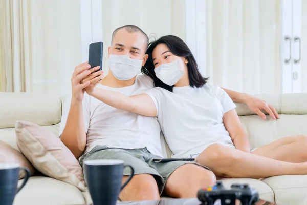 一对年轻夫妇在家中自我隔离时带着面具 用手机合照了一张自拍照片 — 图库照片