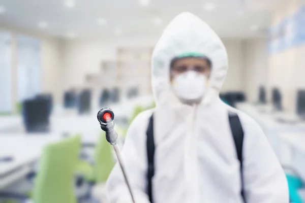 コロナウイルスのパンデミックの間にオフィスで消毒剤を噴霧しながらハズマットスーツを着ている若い男 — ストック写真